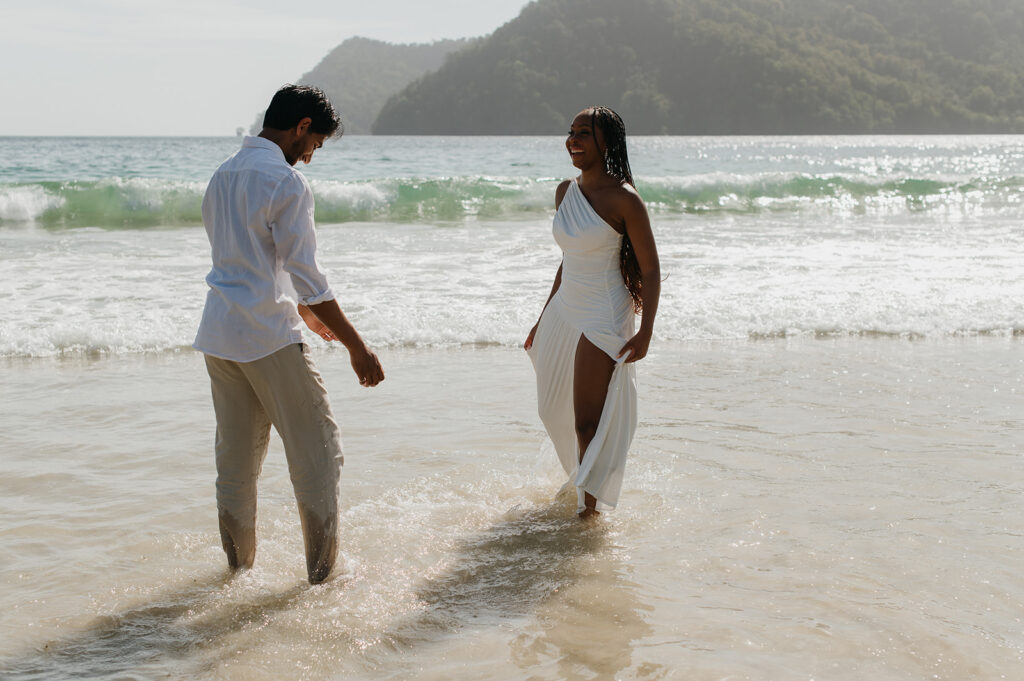 A couple walking hand in hand along the shoreline at Maracas Beach during their engagement session
