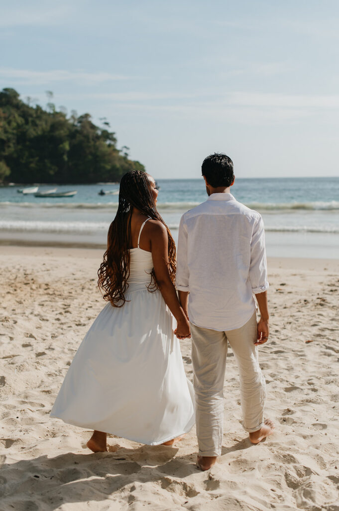 Candid photo of the couple embracing by the ocean with soft golden sunlight around them
