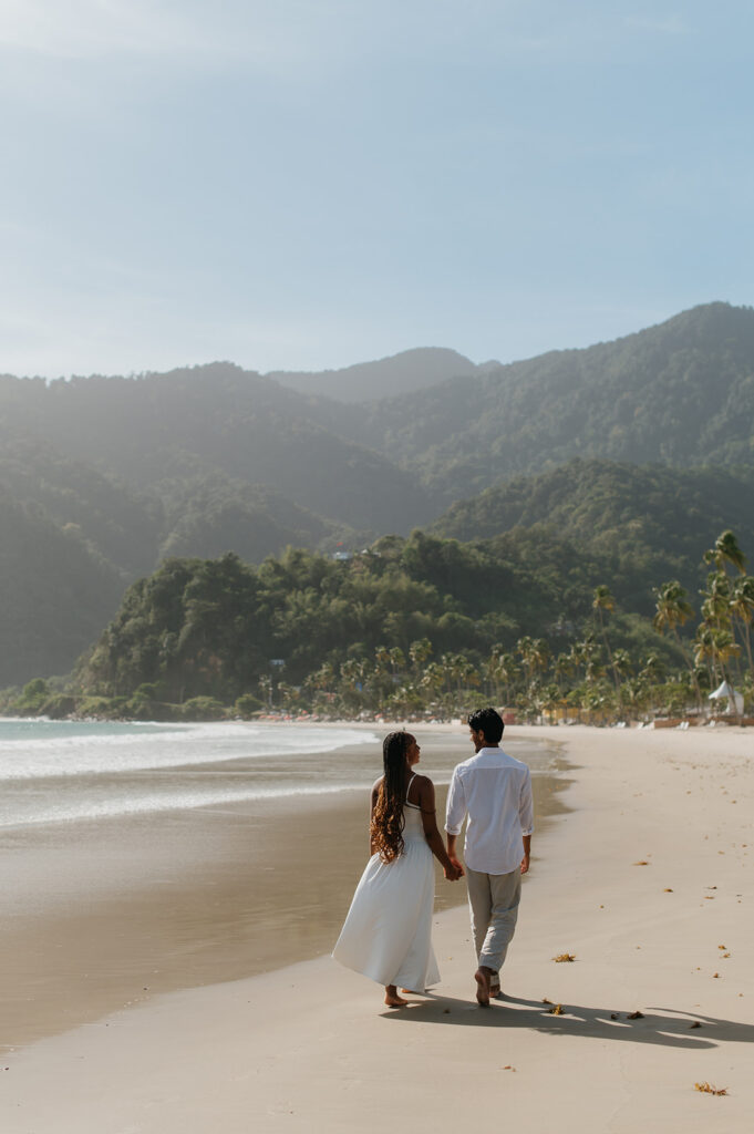 A couple walking hand in hand along the shoreline at Maracas Beach during their engagement session
