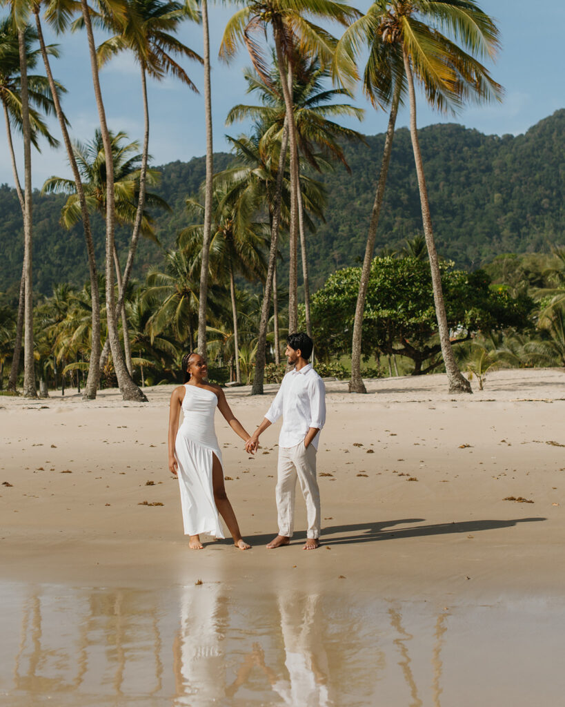 A couple walking hand in hand along the shoreline at Maracas Beach during their engagement session
