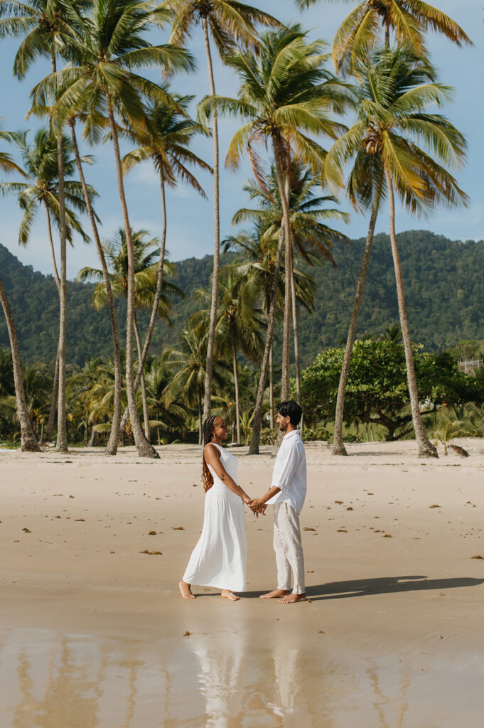 A couple walking hand in hand along the shoreline at Maracas Beach during their engagement session
