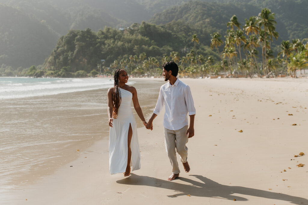 A couple walking hand in hand along the shoreline at Maracas Beach during their engagement session
