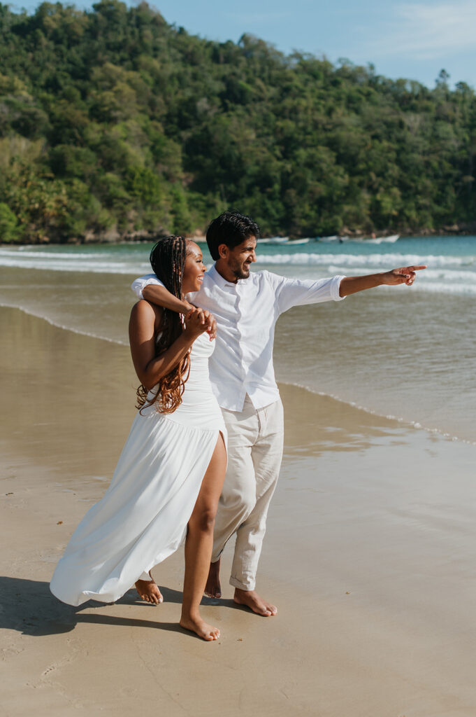 A couple walking hand in hand along the shoreline at Maracas Beach during their engagement session
