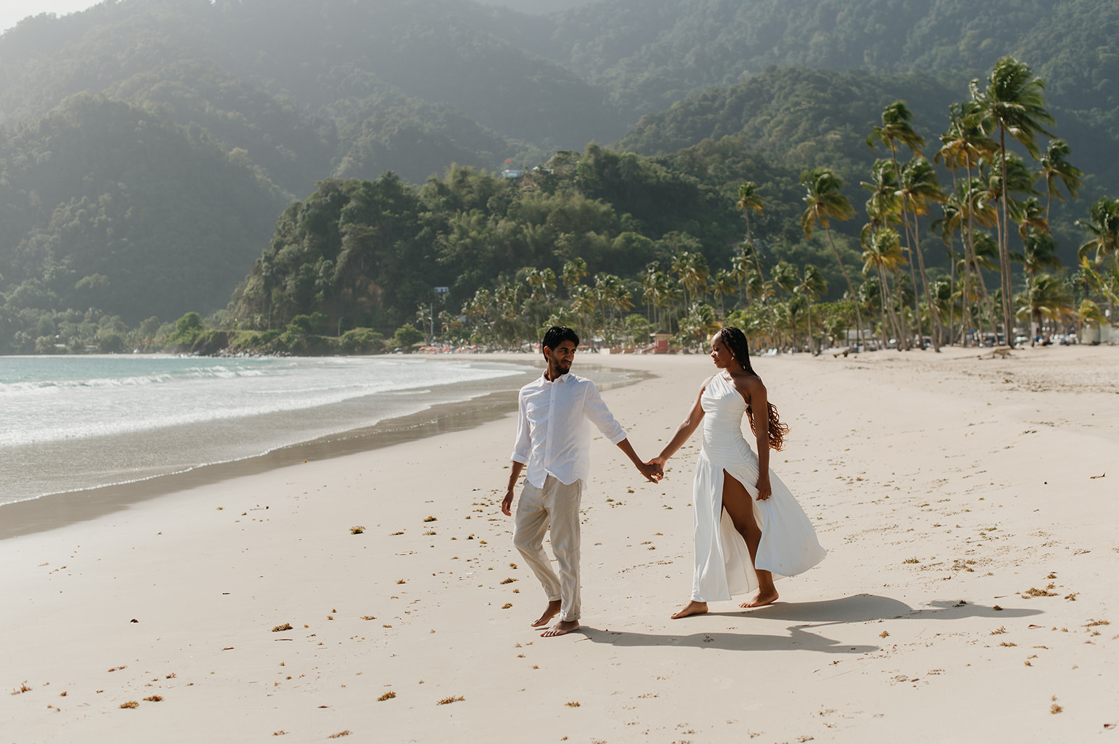 A couple walking hand in hand along the shoreline at Maracas Beach during their engagement session