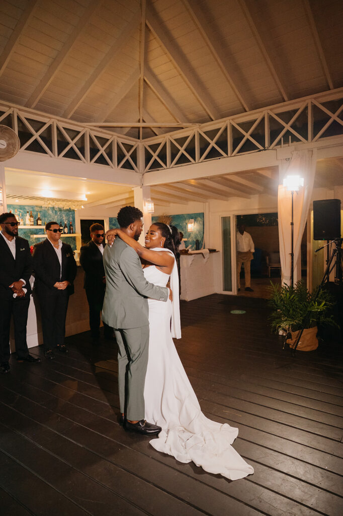 Bride and groom dancing at their beachfront reception under string lights
