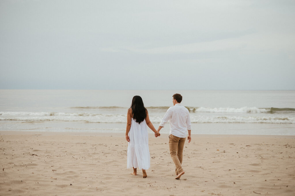 Playful engagement moment as Ross twirls Andrea in the empty stretch of beach during golden hour.
