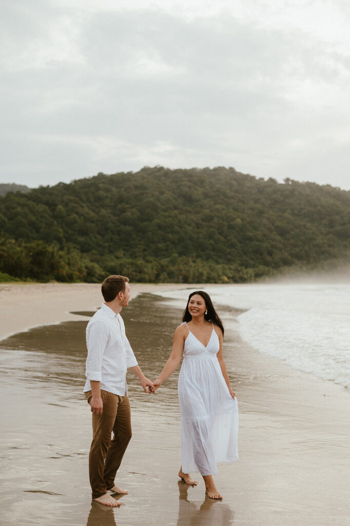 Couple embracing and smiling with the cliffs and ocean views of Las Cuevas Beach in the background.
