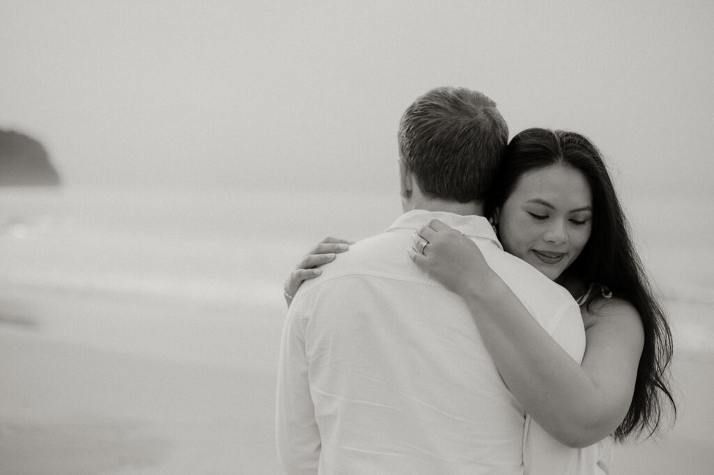 Andrea and Ross holding hands while walking barefoot along the shoreline with soft waves behind them.
