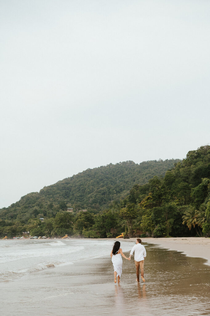 Playful engagement moment as Ross twirls Andrea in the empty stretch of beach during golden hour.
