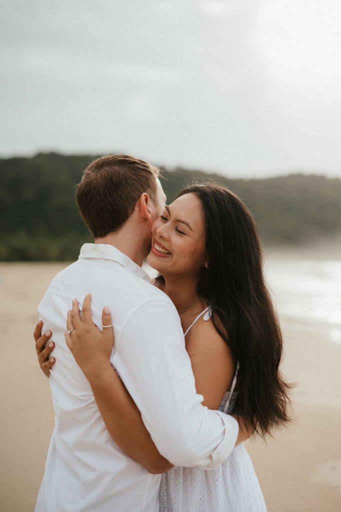 Couple embracing and smiling with the cliffs and ocean views of Las Cuevas Beach in the background.

