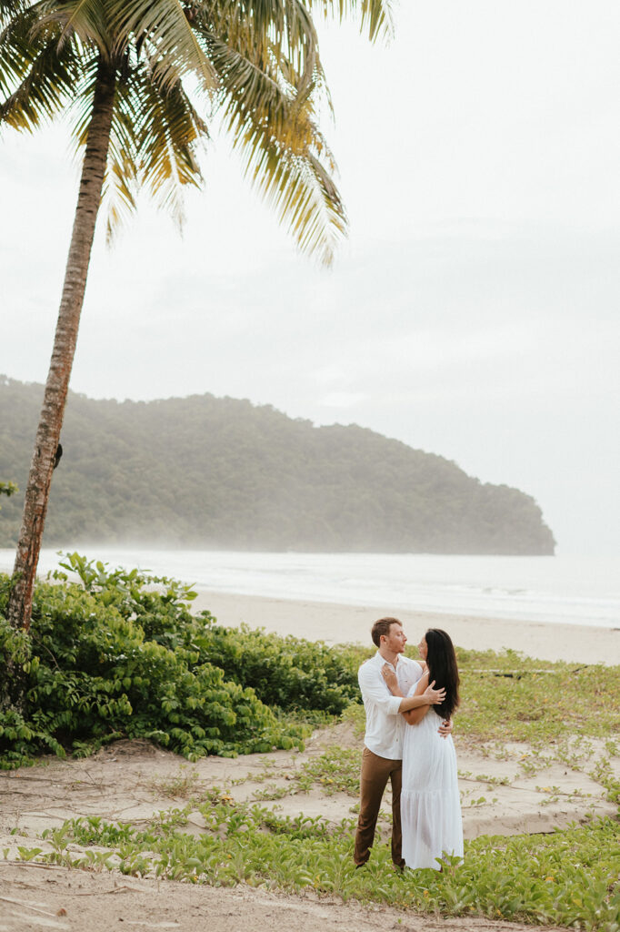 Newly engaged couple laughing during a celebration on the sand at Las Cuevas Beach.

