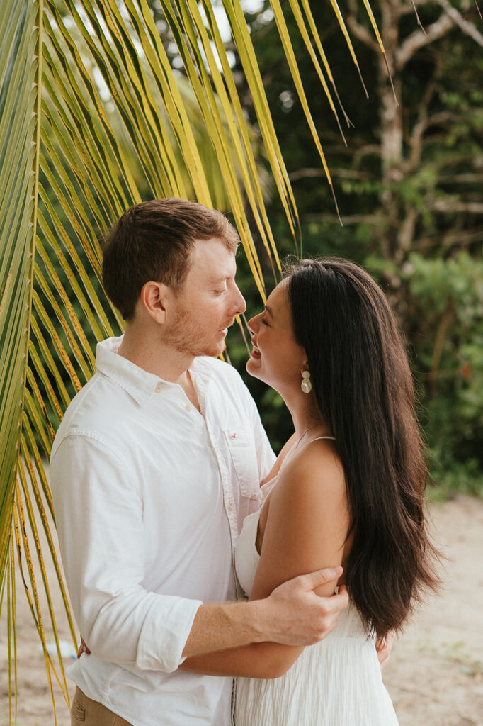 Andrea and Ross holding hands while walking barefoot along the shoreline with soft waves behind them.
