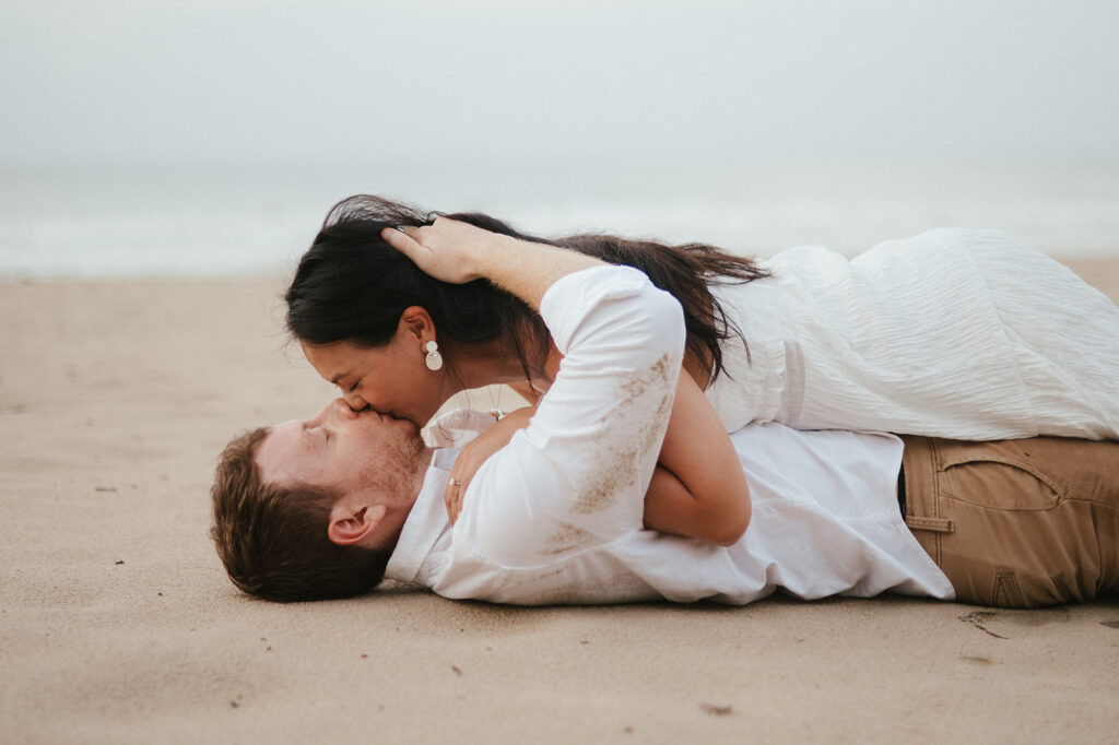 Newly engaged couple laughing during a celebration on the sand at Las Cuevas Beach.

