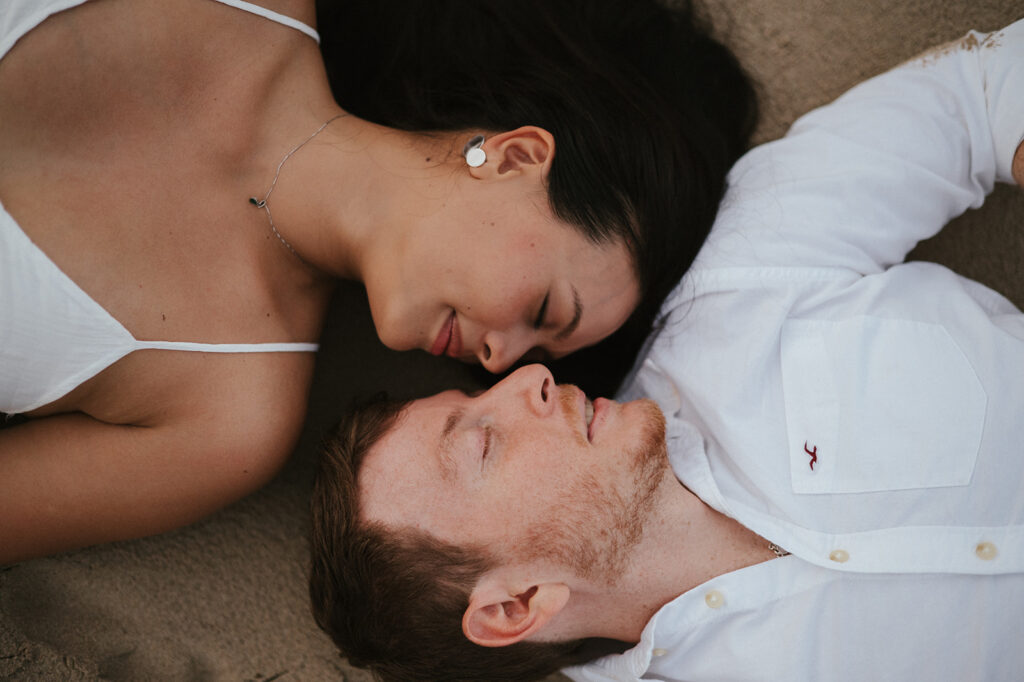 Newly engaged couple laughing during a celebration on the sand at Las Cuevas Beach.
