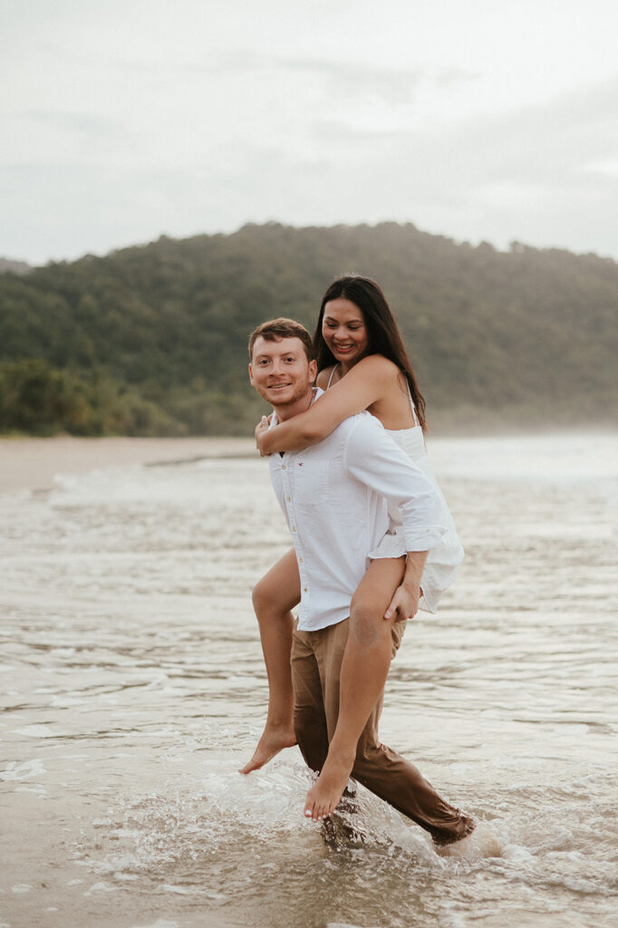 Newly engaged couple laughing during a celebration on the sand at Las Cuevas Beach.
