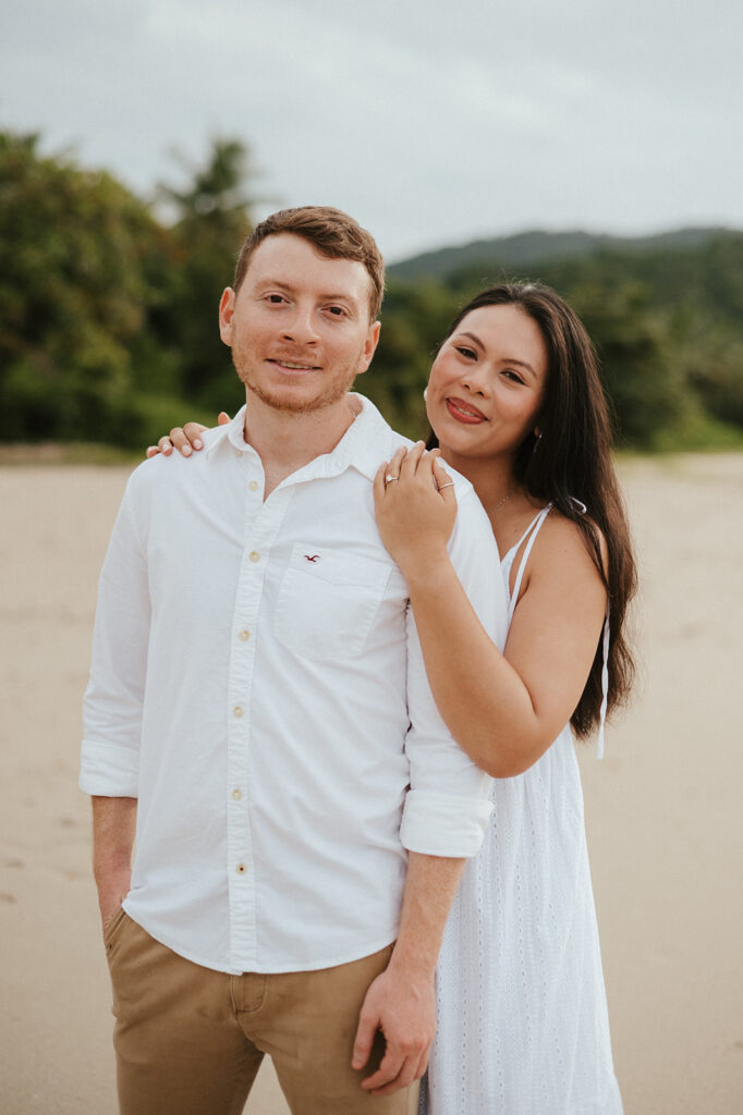 Couple embracing and smiling with the cliffs and ocean views of Las Cuevas Beach in the background.
