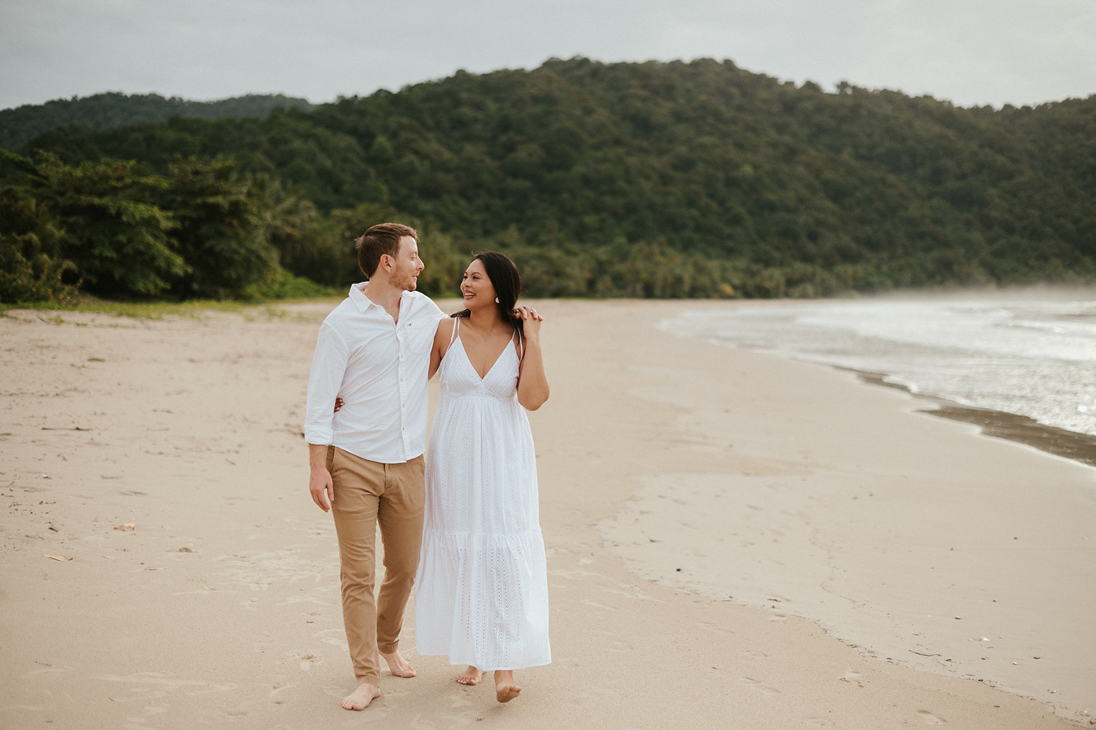 Newly engaged couple laughing and spraying champagne during a celebration on the sand at Las Cuevas Beach.
