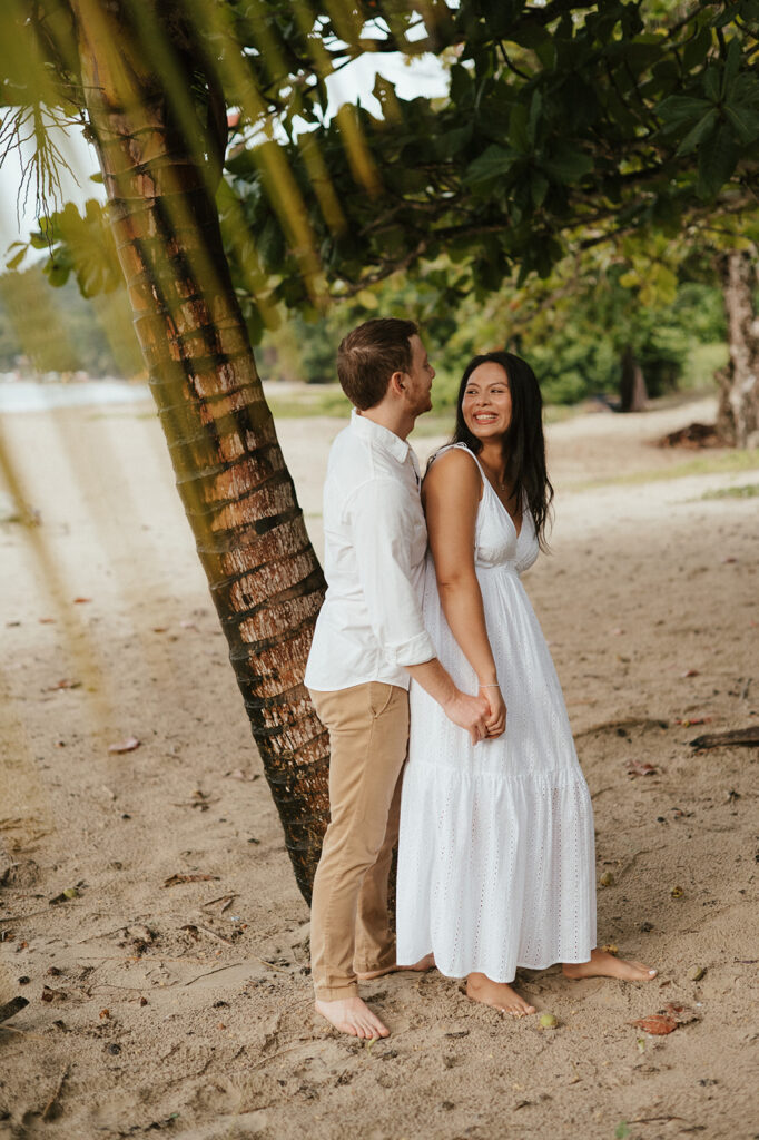 Andrea and Ross holding hands while walking barefoot along the shoreline with soft waves behind them.
