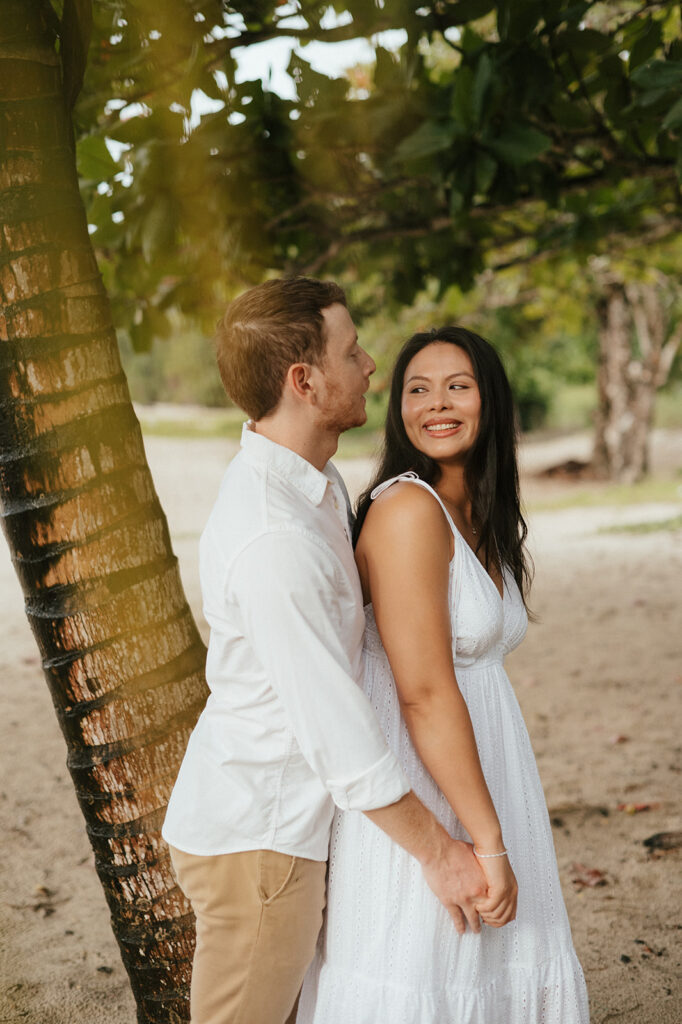 Andrea and Ross holding hands while walking barefoot along the shoreline with soft waves behind them.
