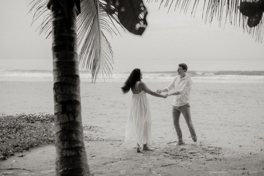 Couple embracing and smiling with the cliffs and ocean views of Las Cuevas Beach in the background.
