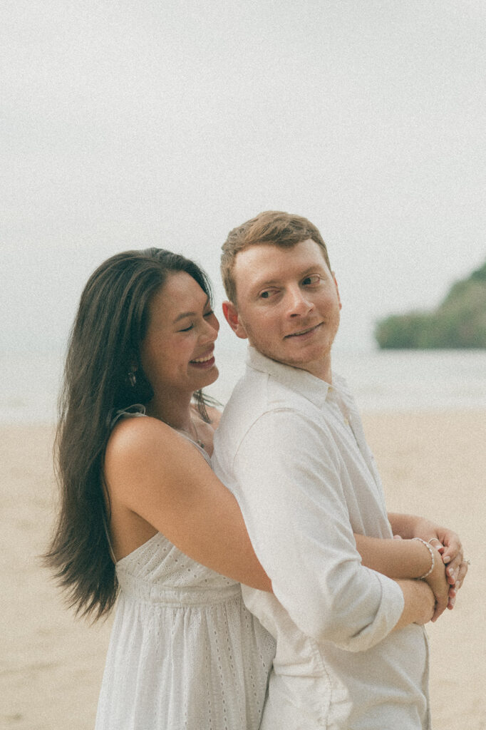 Couple embracing and smiling with the cliffs and ocean views of Las Cuevas Beach in the background.
