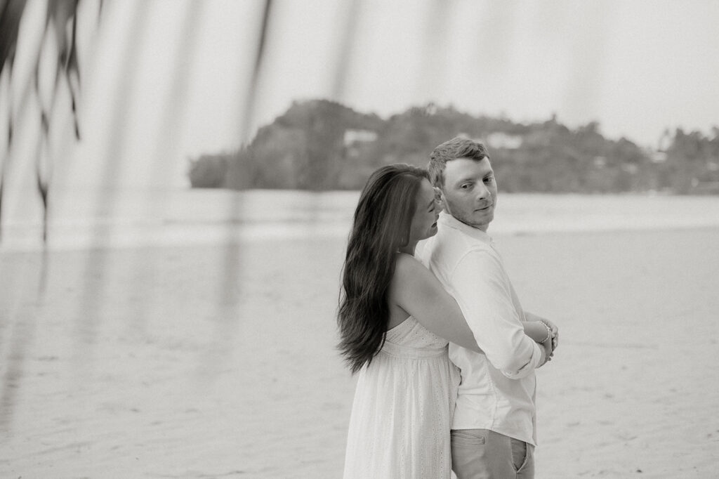 Couple embracing and smiling with the cliffs and ocean views of Las Cuevas Beach in the background.
