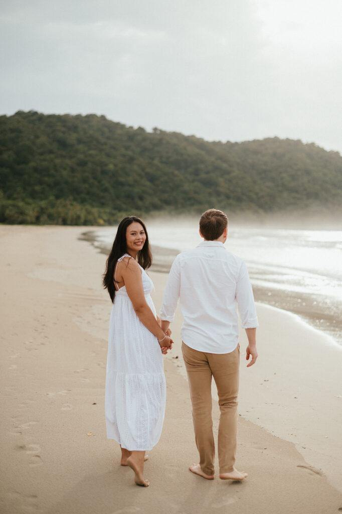 Playful engagement moment as Ross twirls Andrea in the empty stretch of beach during golden hour.
