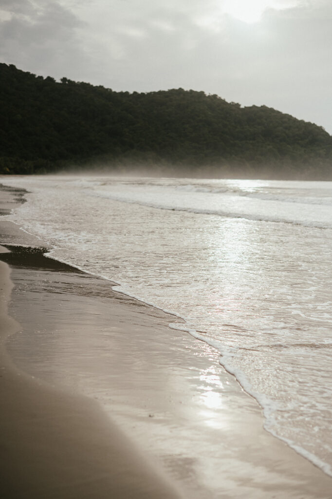 Couple embracing and smiling with the cliffs and ocean views of Las Cuevas Beach in the background.
