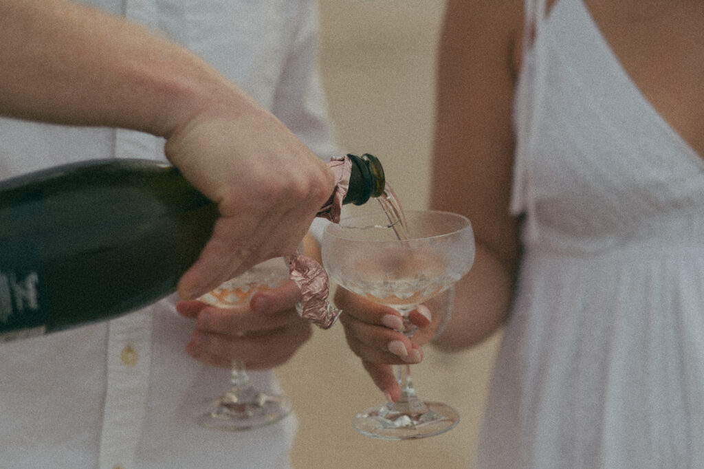 Newly engaged couple laughing and spraying champagne during a celebration on the sand at Las Cuevas Beach.
