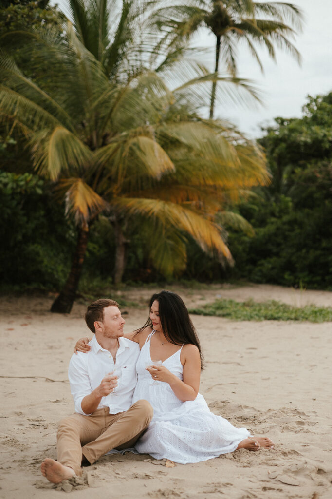 Andrea and Ross holding hands while walking barefoot along the shoreline with soft waves behind them.
