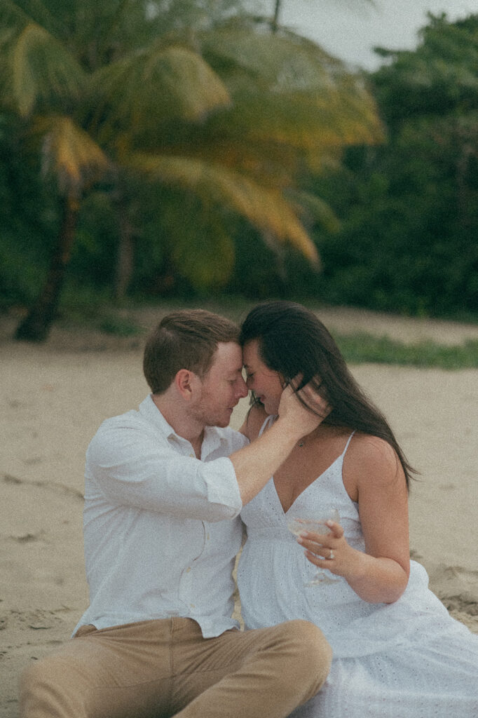 Newly engaged couple laughing and spraying champagne during a celebration on the sand at Las Cuevas Beach.
