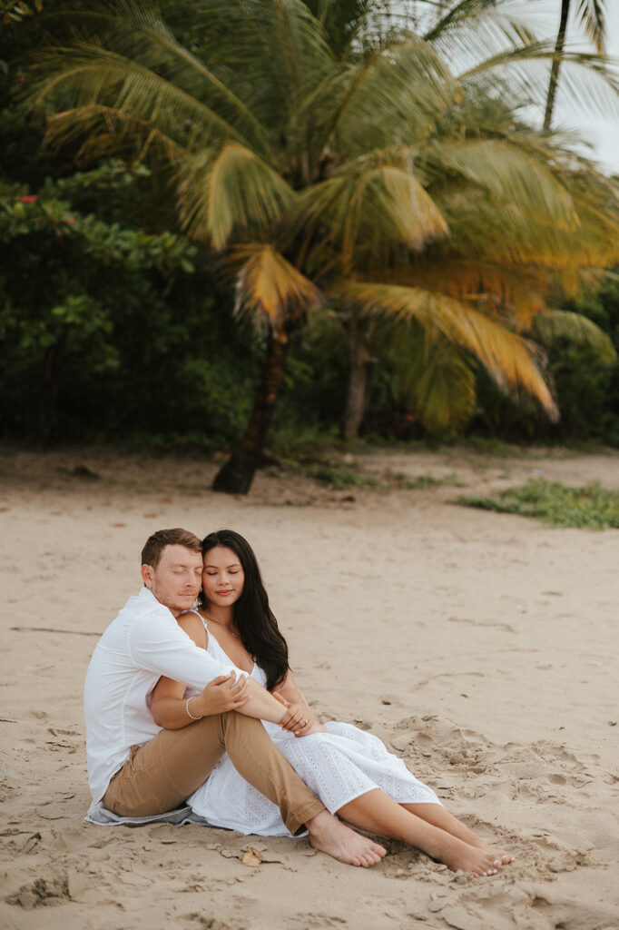 Couple embracing and smiling with the cliffs and ocean views of Las Cuevas Beach in the background.
